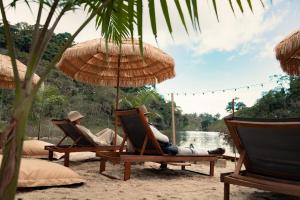 dos personas sentadas en sillas bajo sombrillas en una playa en BubbleSky Glamping Guatapé en Guatapé