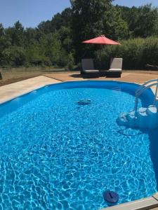 a large blue swimming pool with an umbrella and chairs at Peaceful, comfortable retreat with pool in Montcléra