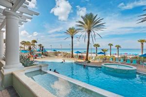 een zwembad in een resort met palmbomen en de oceaan bij Boardwalk 1406 in Panama City Beach