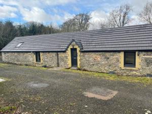 een stenen gebouw met een zwart dak en een deur bij West Loch Farm Bothy in Peebles