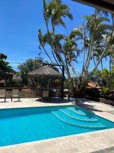 a swimming pool with a table and a umbrella and palm trees at Casa 10 suítes, até 64 pessoas, Praia Ferradura in Búzios