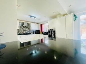a kitchen with white cabinets and a black floor at Spacious 5 Bedroom house with free parking by Hostaguest in Luton