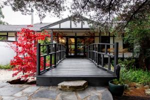 uma passagem de madeira que leva a uma casa com folhas vermelhas em Shizuka Ryokan Japanese Country Spa & Wellness Retreat em Hepburn Springs