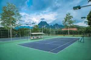 una pista de tenis con árboles y montañas al fondo en VResort Kim Boi - Hoa Binh en Hòa Bình