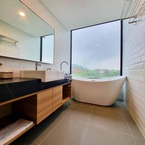 La salle de bains est pourvue d'une baignoire, d'un lavabo et d'une fenêtre. dans l'établissement Villa Daun at Dago Village, à Bandung