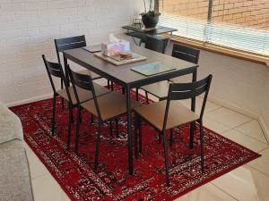 a dining room table with chairs on a red rug at Tuggeranong Short Stay #07 - Sleeps 6 in Tuggeranong