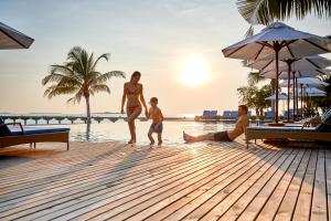 a woman and a child walking on a dock at the beach at ROBINSON NOONU - All Inclusive in Manadhoo