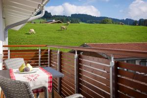 una mesa y sillas en un balcón con vacas en un campo en 5 Sterne Ferienwohnung Hochgratblick mit Schwimmbad und Sauna en Oberstaufen
