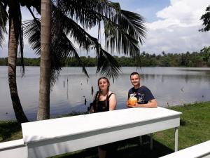 un hombre y una mujer parados junto a una mesa frente a un lago en Mario River Villa en Ambalangoda