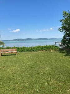 a park bench sitting in the grass near the water at Attila Beach Boglár in Balatonboglár