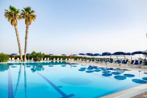 une grande piscine avec des chaises et des palmiers dans l'établissement Hotel Village Paradise, à Mandatoriccio Marina