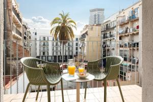 Duas cadeiras e uma mesa numa varanda com dois copos de sumo de laranja em Aspasios Las Ramblas Apartments em Barcelona