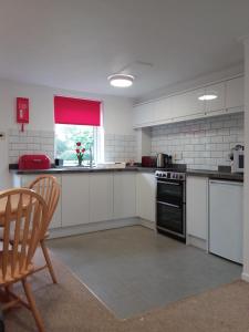 a kitchen with white cabinets and a red window at Salty Smiles Cottage in Penzance