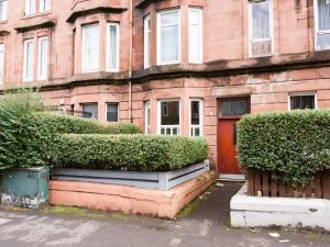 a brick building with a red door and some bushes at PER7-FM · Nice 1 Bed Ground Floor Flat, near Cessnock Subway in Glasgow