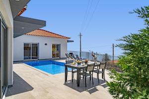 a patio with a table and chairs next to a pool at Villa Calhetascape by Villa Plus in Estreito da Calheta