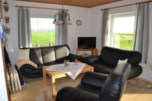 ein Wohnzimmer mit schwarzen Ledermöbeln und einem Tisch in der Unterkunft Ferienhof Nickelswarft Fewo 2 in Poppenbüll