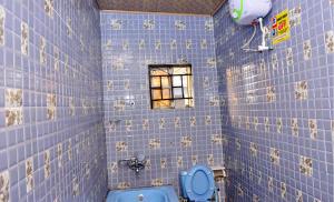 La salle de bains est pourvue de carrelage bleu, de toilettes et d'une fenêtre. dans l'établissement The Agore Hotels and Suites Ltd, à Awoyaya