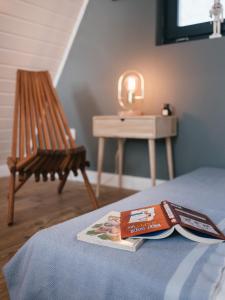 a book on a bed with a chair and a table at Kanyar - Nordic Cabin in Zebegény