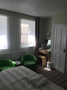 a bedroom with a bed and two green chairs and a desk at Tregonholme Hotel in Bournemouth
