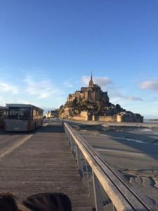 un autobús en un paseo marítimo con un castillo en el fondo en Maison familiale à 10 min du Mont Saint Michel en Pontorson