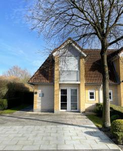 a yellow house with a tree and a driveway at Vakantiehuis met Luxe Tuin dichtbij het strand in Kamperland