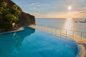 a swimming pool next to the ocean at sunset at Mogan Princess & Beach Club in Taurito