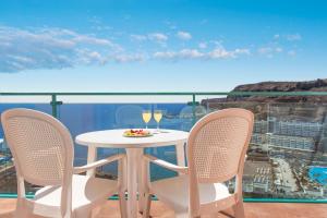 a table with two chairs and wine glasses on a balcony at Mogan Princess & Beach Club in Taurito