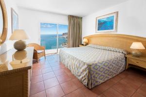 a bedroom with a bed and a desk and a window at Mogan Princess & Beach Club in Taurito