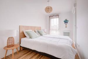 a white bedroom with a large bed and a chair at Très belle appartement haut standing in Lacanau-Océan
