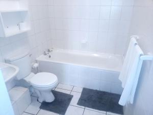 a white bathroom with a toilet and a bath tub at Goshen Place in Cape Town
