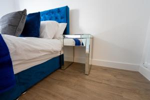 uma cama com uma cabeceira azul e uma mesa de vidro em Newly Built Spacious Apartment easily accessible to Luton Airport, Town centre and station em Luton
