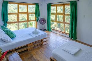 two beds in a room with green curtains and windows at Hostal Mama Tayrona in Santa Marta