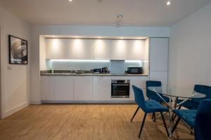 uma cozinha com uma mesa de vidro e cadeiras azuis em Newly Built Spacious Apartment easily accessible to Luton Airport, Town centre and station em Luton
