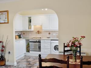 a kitchen with white cabinets and a table with flowers at Little Coombe in Ashbury