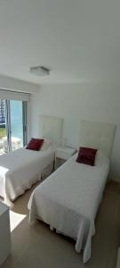 Duas camas num quarto branco com uma janela em Jose Luis Arenas del Mar Torre 1 em Punta del Este