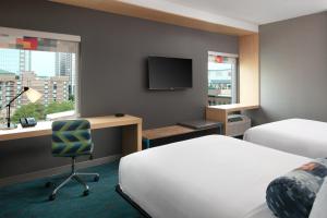 a hotel room with two beds and a desk and a television at Aloft Louisville Downtown in Louisville