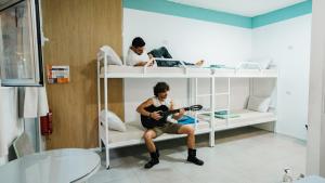 mężczyzna siedzący na łóżku piętrowym grający na gitarze w obiekcie Marina Ben Gurion Hostel w Tel Awiwie