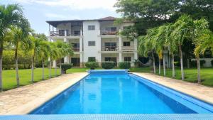 una piscina frente a una casa con palmeras en Condo Golf B3 F3 Hacienda Iguana, en Tola
