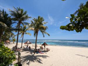 a beach with palm trees and people sitting on the sand at Le Laïlana in Sainte-Anne