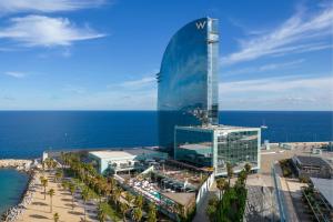 a tall glass building next to a beach with the ocean at W Barcelona in Barcelona