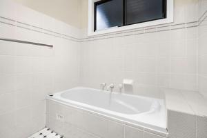 La salle de bains blanche est pourvue d'une baignoire et d'une fenêtre. dans l'établissement Baileys Retreat, à Leura