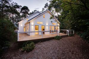una pequeña casa blanca con una gran terraza de madera en White Cottage, en Wentworth Falls
