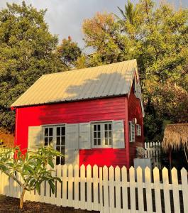 a red shed behind a white fence at La Petite Kaz Dans la Savane in Fleurimont