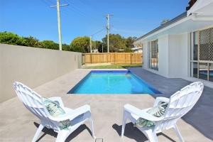 two white chairs sitting next to a swimming pool at Beautiful Beach House in the Heart of Town in Coolum Beach