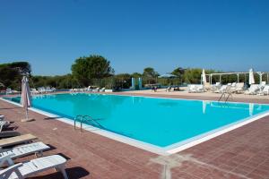 a large blue swimming pool with chairs and umbrellas at Camping Village S'Ena Arrubia in Arborea 