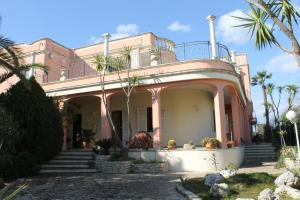 Villa la Bifora by Salento com في كاسترينيانو دل كابو: منزل وردي أمامه أشجار نخيل
