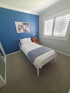 een slaapkamer met een bed met een blauwe muur bij Located between picturesque Lake Illawarra and Windang beach in Windang