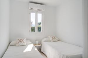 twee bedden in een witte kamer met een raam bij Cas Buc - Villa con piscina a pasitos del mar in Cala Blanca +11 foto's