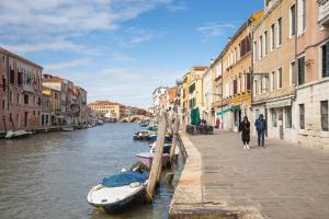 una mujer caminando por una calle junto a un canal con barcos en Appartamento Cà Gamba, Cannaregio alle Guglie en Venecia