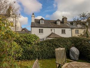 a large white house with a hedge and a chair at Early Mist Cottage in Newton Abbot